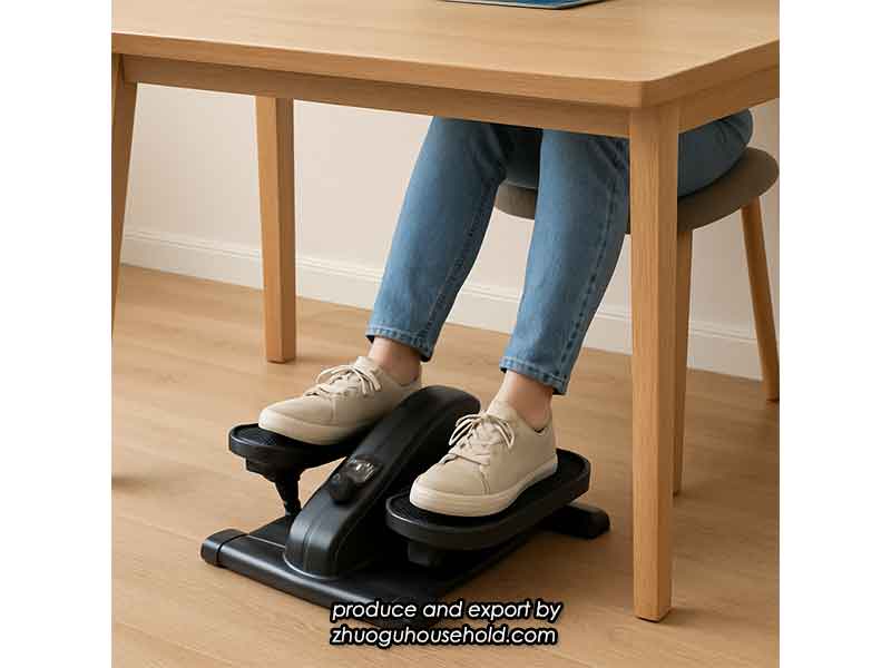 A clean, simple photo of an under desk elliptical placed neatly under a standard home office desk. The user's feet (in casual shoes or socks) are on the pedals.